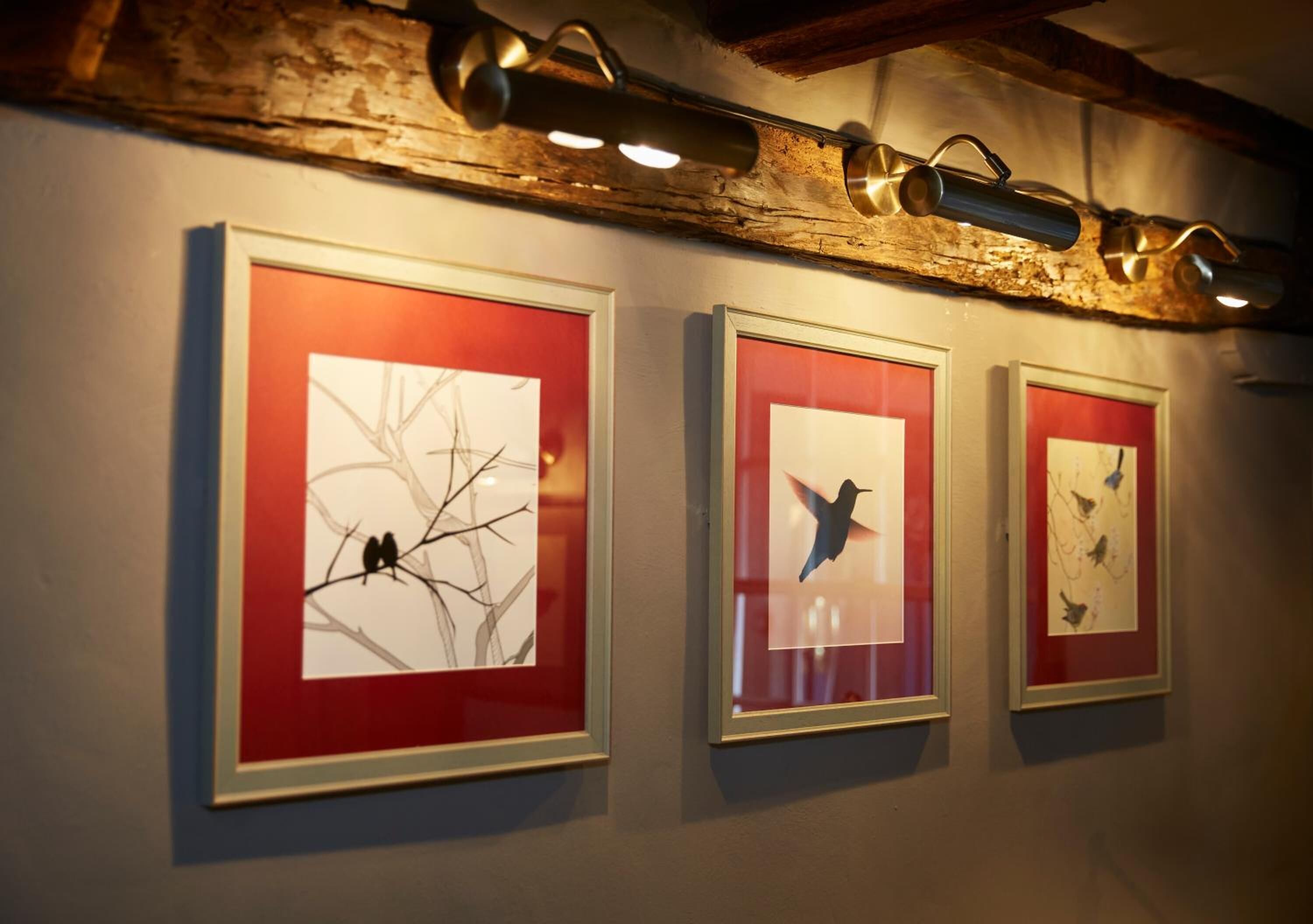 Three framed artworks on a wall with a rustic wooden beam above.