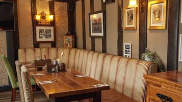 Un restaurante con mesa de madera, asientos tipo cabina a rayas y cuadros en las paredes.