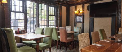 Un restaurant avec des tables et des chaises en bois, de grandes fenêtres et un tapis à motifs.