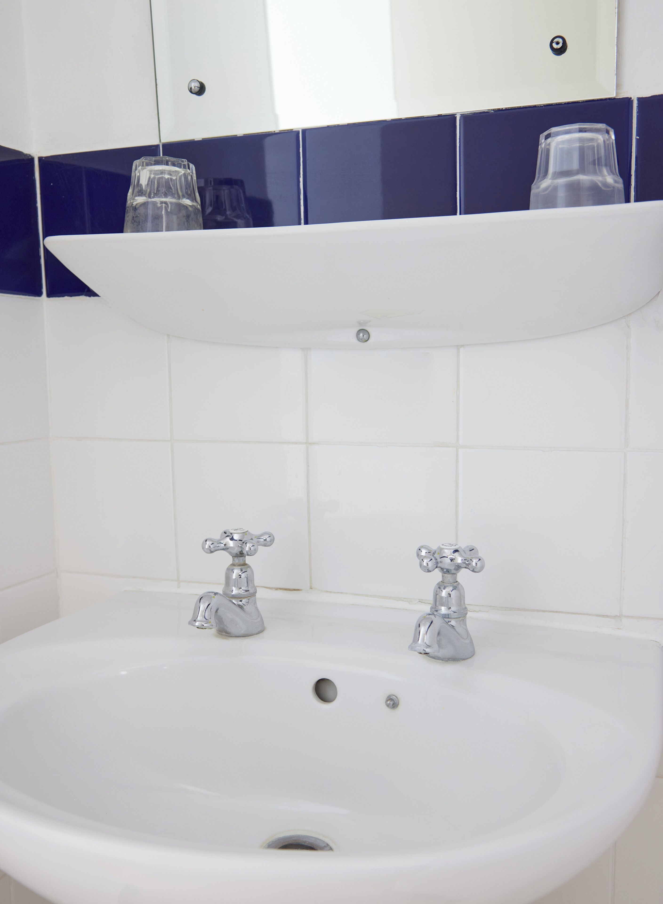 Un baño con un lavamanos blanco, dos grifos y un espejo encima.