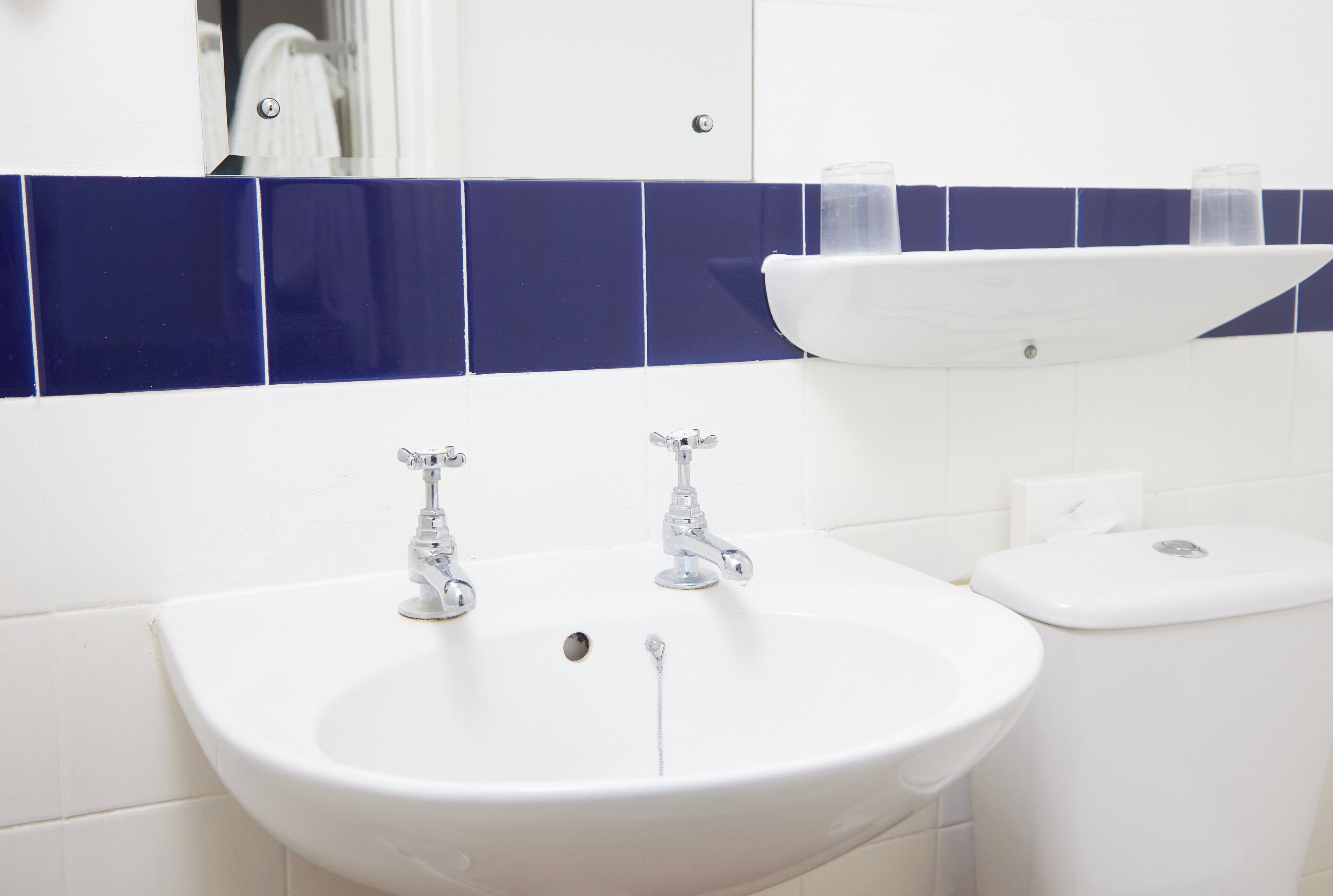 A bathroom with a white sink, two faucets, and a toilet.