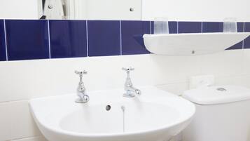 A bathroom with a white sink, two faucets, and a toilet.