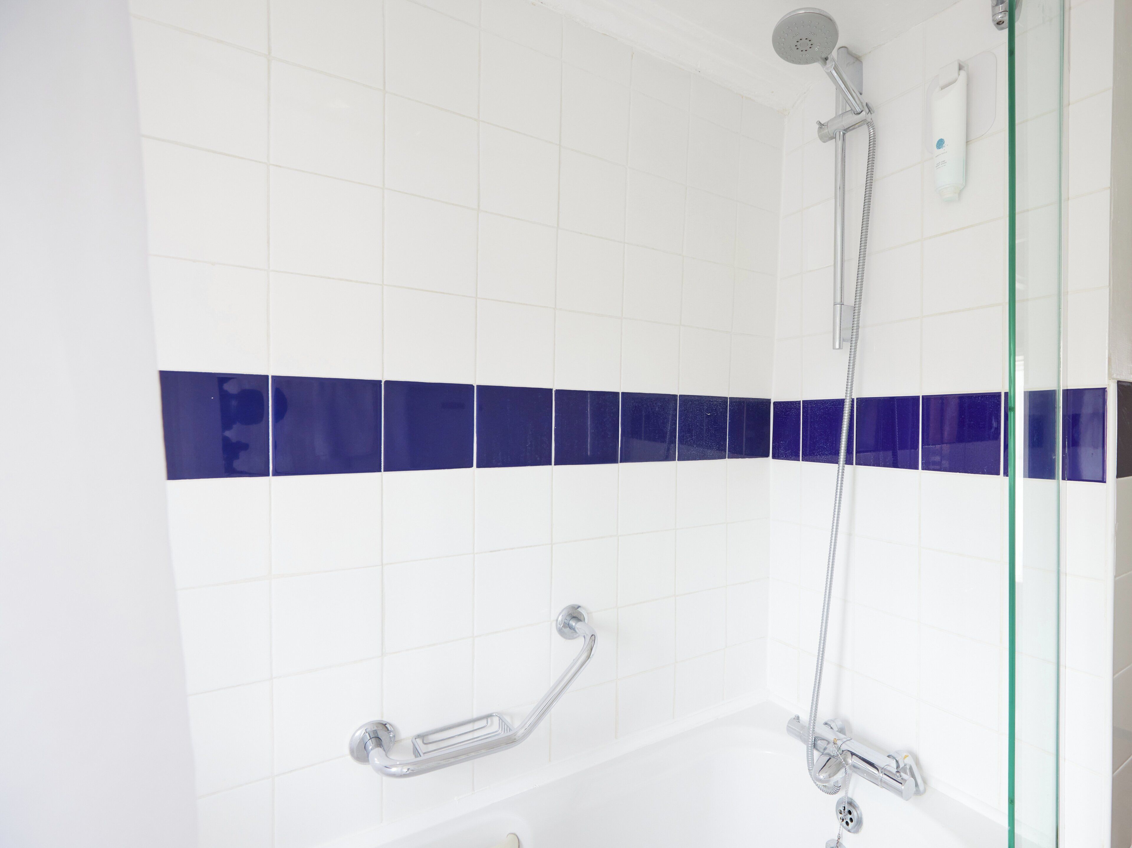 Ein modernes Badezimmer mit weißen Fliesen, einem blauen Akzentstreifen, einer Duschkabine aus Glas und einer Handbrause.