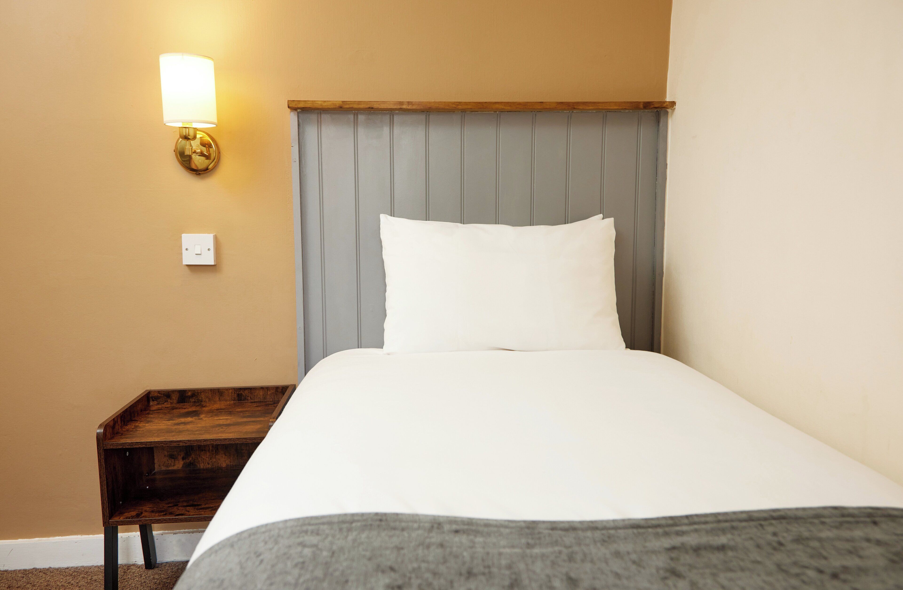 A hotel room with a bed, a nightstand, a lamp, and a wall socket.
