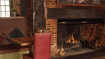 A cozy seating area with a fireplace, a red chair, and a wooden table.