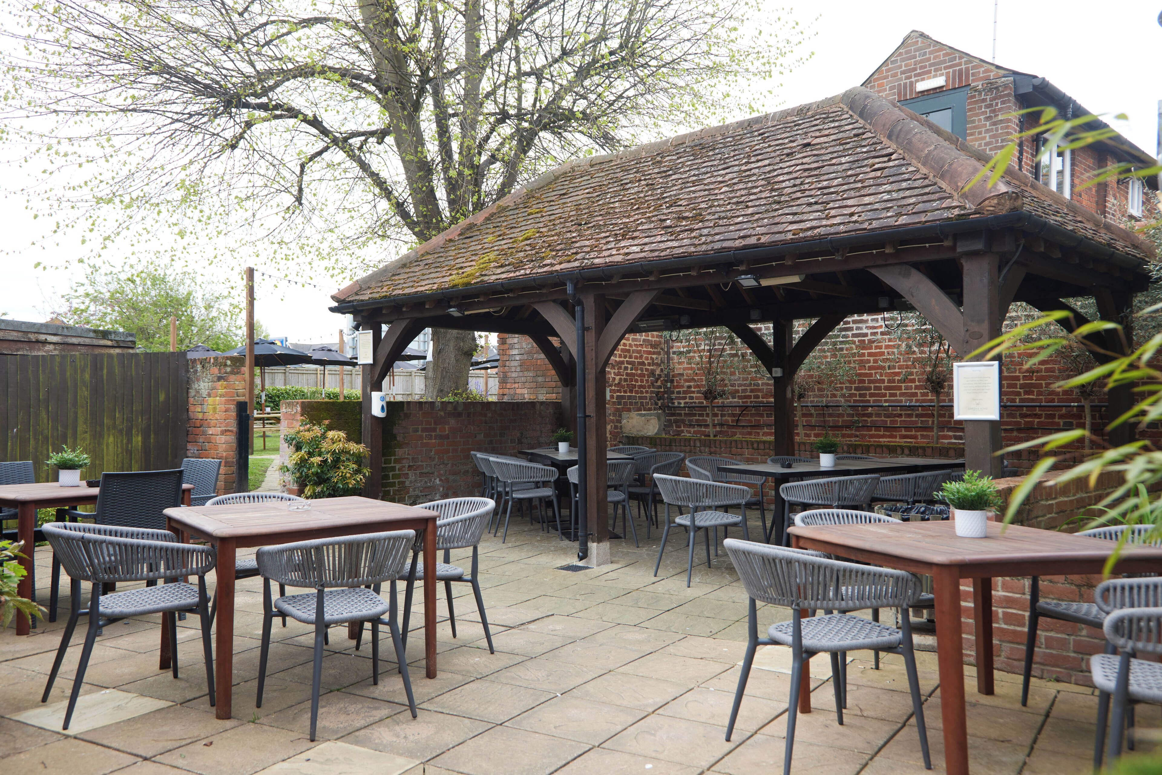 An outdoor patio area with brick walls, a wooden pergola, and multiple tables and chairs.