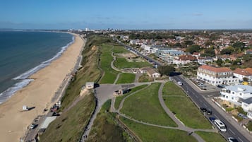 An aerial view of a coastal town with a beach, residential buildings, and a road with vehicles.