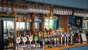 A bar with multiple beer taps, a variety of bottles, and hanging glasses. - Commodore Hotel Bournemouth by Greene King Inns (Bournemouth)