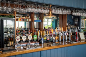 A bar with multiple beer taps, a variety of bottles, and hanging glasses.