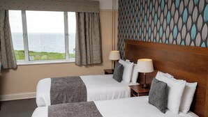 A hotel room with two beds, a view of the sea, patterned wallpaper, and a wooden headboard. - Commodore Hotel Bournemouth by Greene King Inns (Bournemouth)