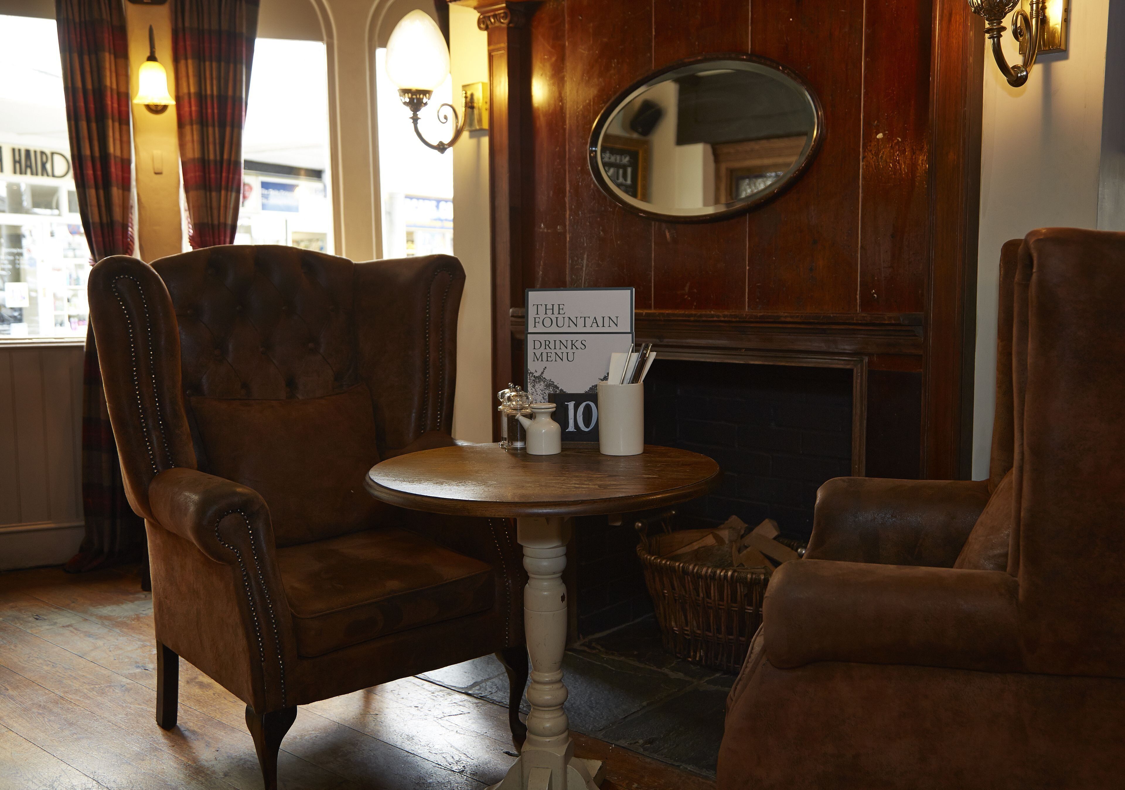A cozy room with a fireplace, a table with a menu sign, and two leather armchairs.