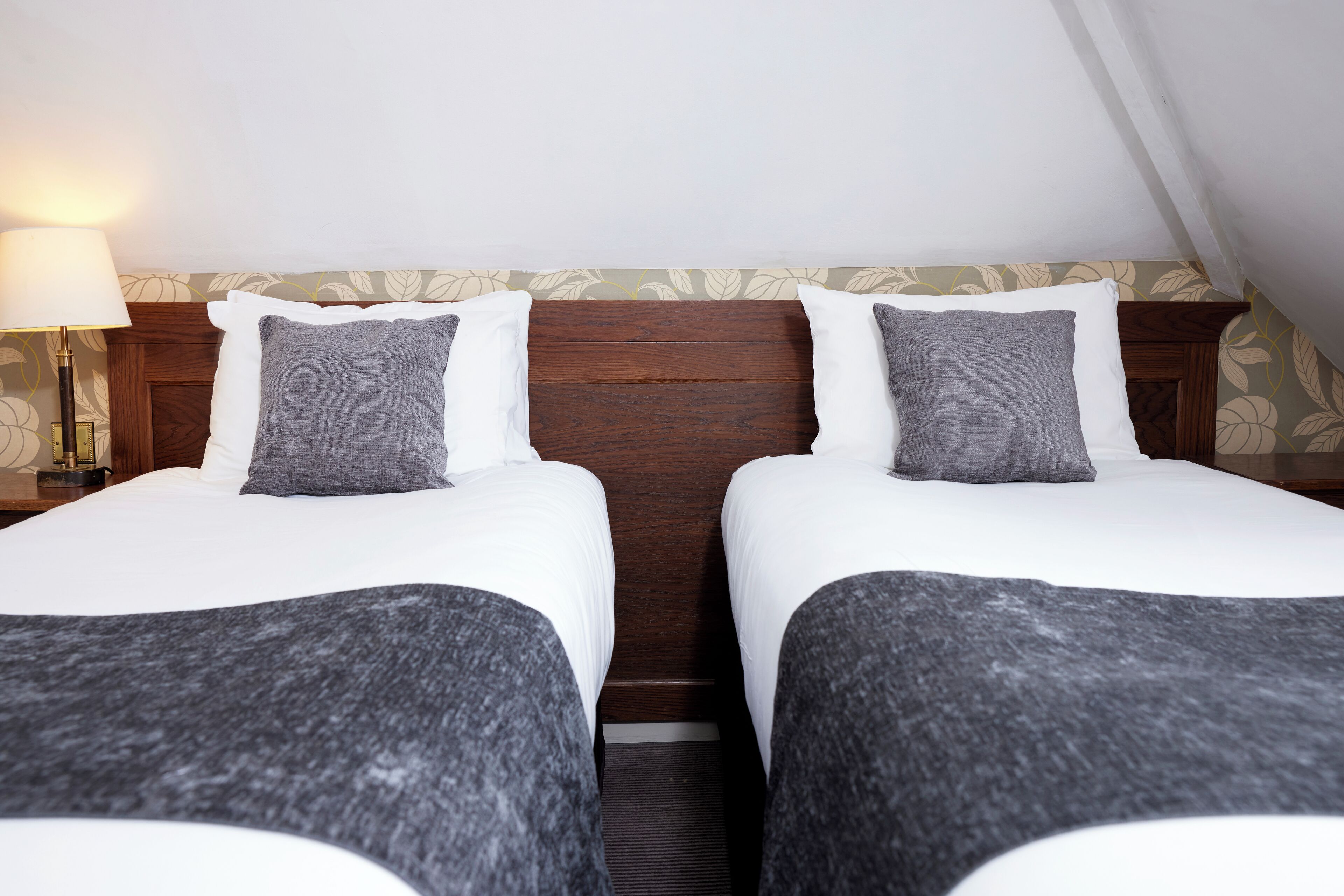 Une chambre double avec deux lits, une tête de lit en bois, une table de chevet avec une lampe et un papier peint à motifs floraux.