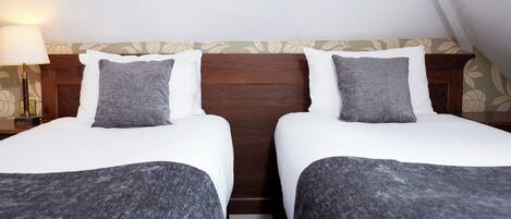 Une chambre double avec deux lits, une tête de lit en bois, une table de chevet avec une lampe et un papier peint à motifs floraux.