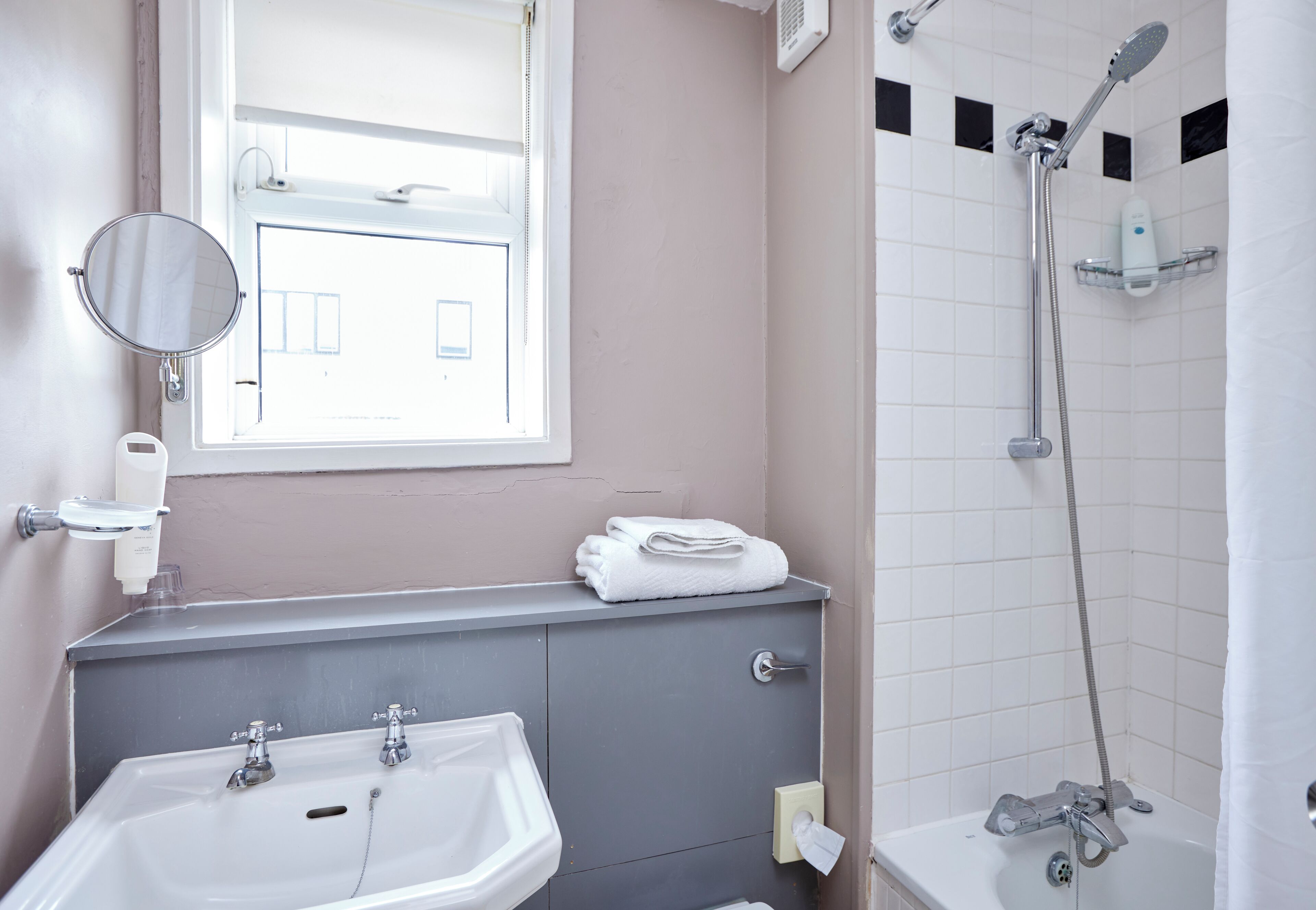 A bathroom with a sink, mirror, towel rack, and shower.