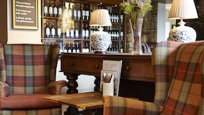 Un'accogliente zona con posti a sedere, poltrone a quadri e un tavolo di legno, una dispensa per vini sullo sfondo e un cartello con scritto "THE DOG HOUSE".