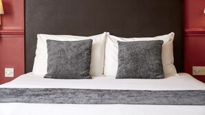 Un letto rifatto con cuscini bianchi e grigi, una testiera scura e una coperta grigia.