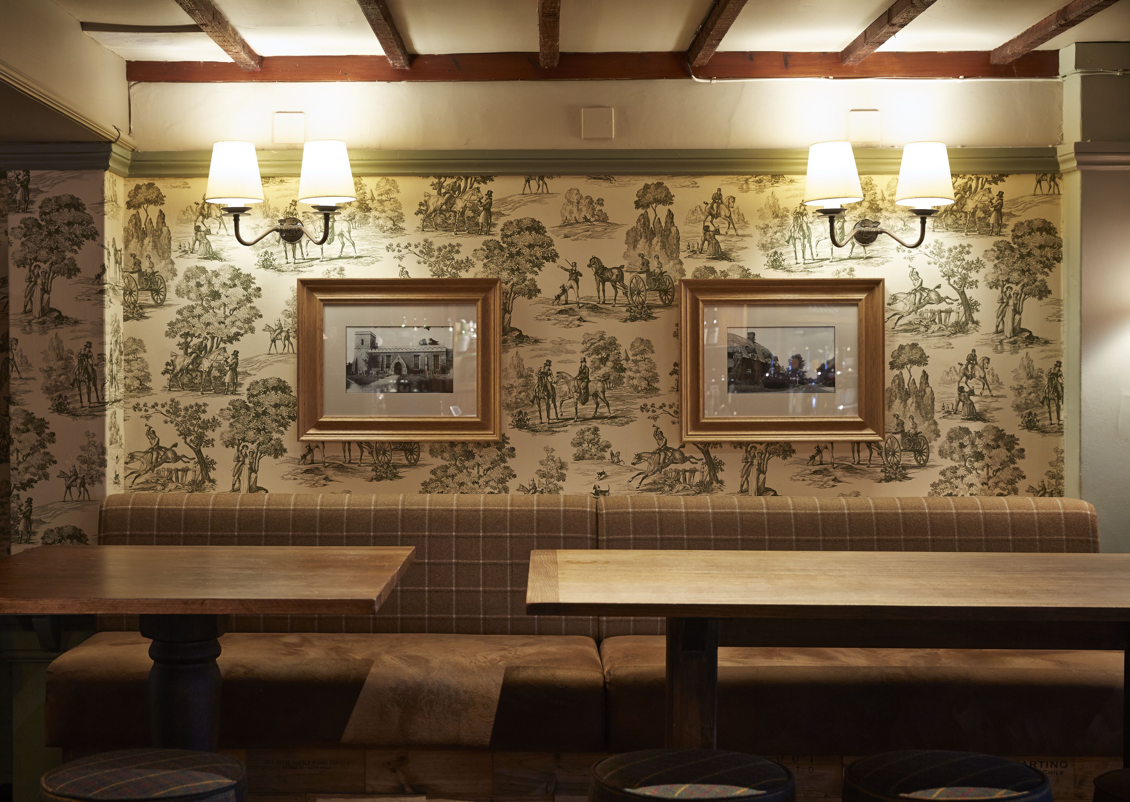 Interior de un restaurante con una zona de estar con bancos de madera, cuadros en la pared y dos lámparas de pared.