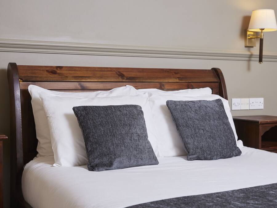 A neatly made bed with white and gray pillows, a wooden headboard, and a wall-mounted lamp.