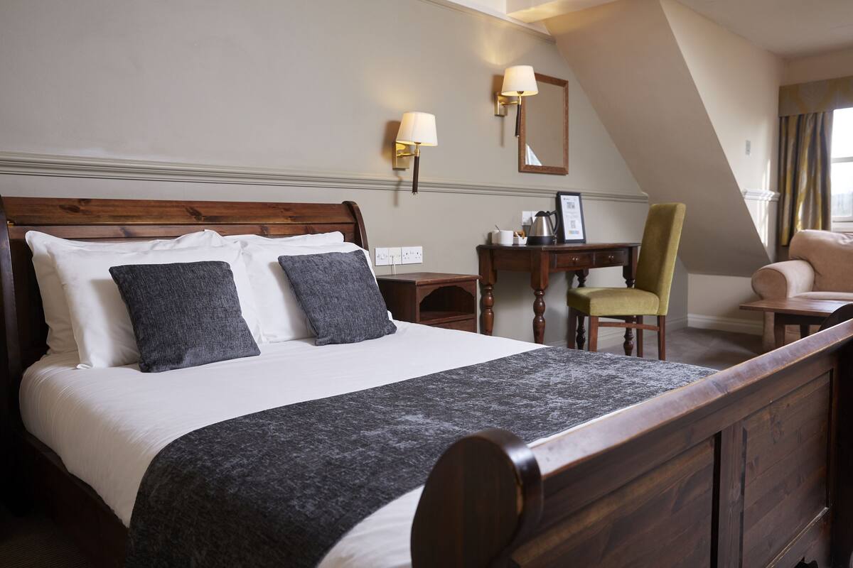 A neatly made bed with a wooden headboard, a desk with a chair, and a lamp.