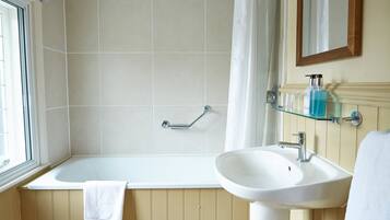 Een badkamer met een bad, een wastafel en een glazen plank met toiletartikelen.