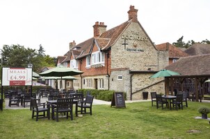 Un área de estar al aire libre con mesas y sillas frente a un edificio que dice "The Doc House Greene King".
