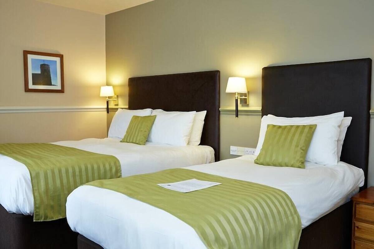 Two twin beds with green bedding, a framed picture on the wall, and two wall-mounted lamps.