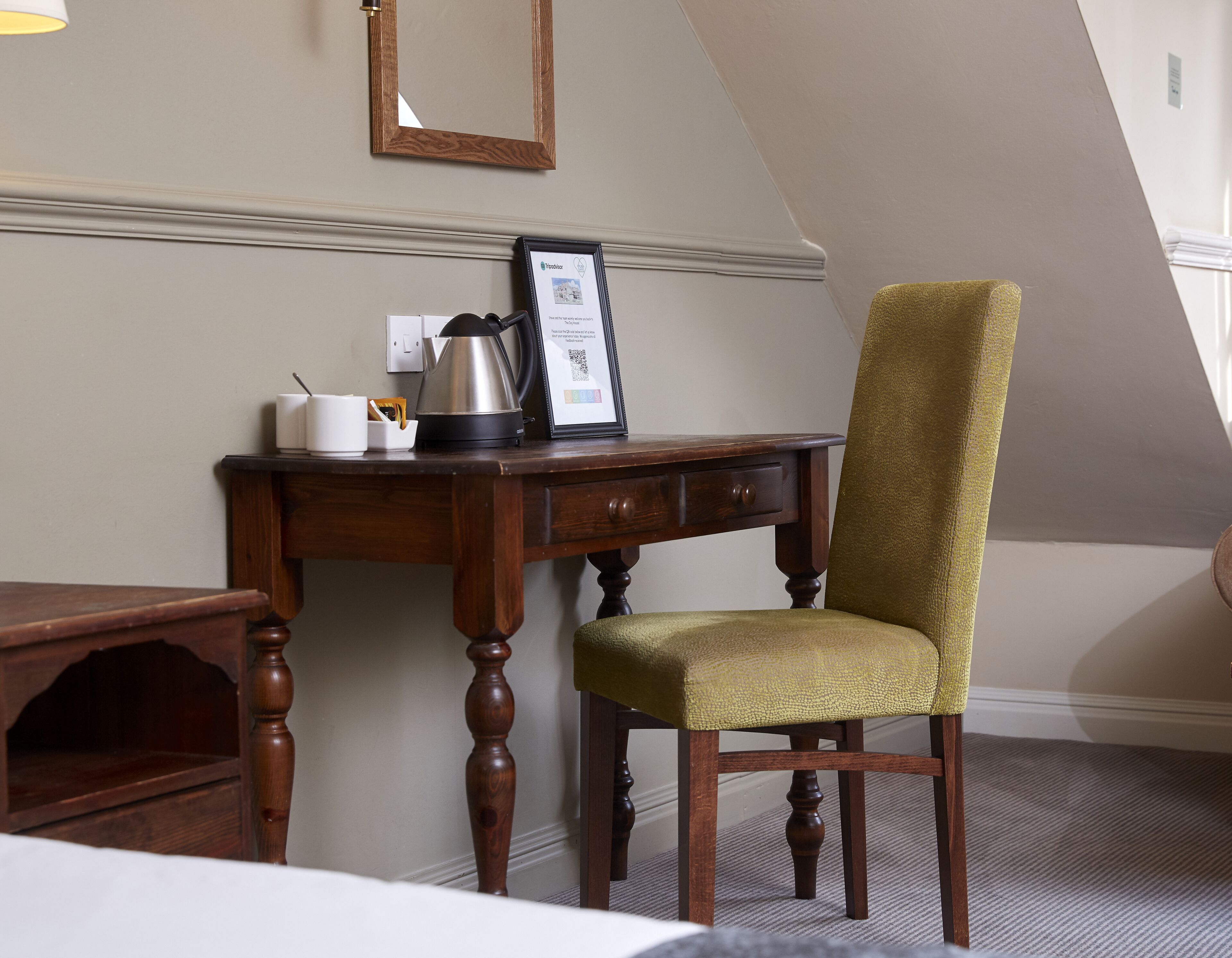 A hotel room with a wooden desk, a chair, a framed certificate, and a kettle.
