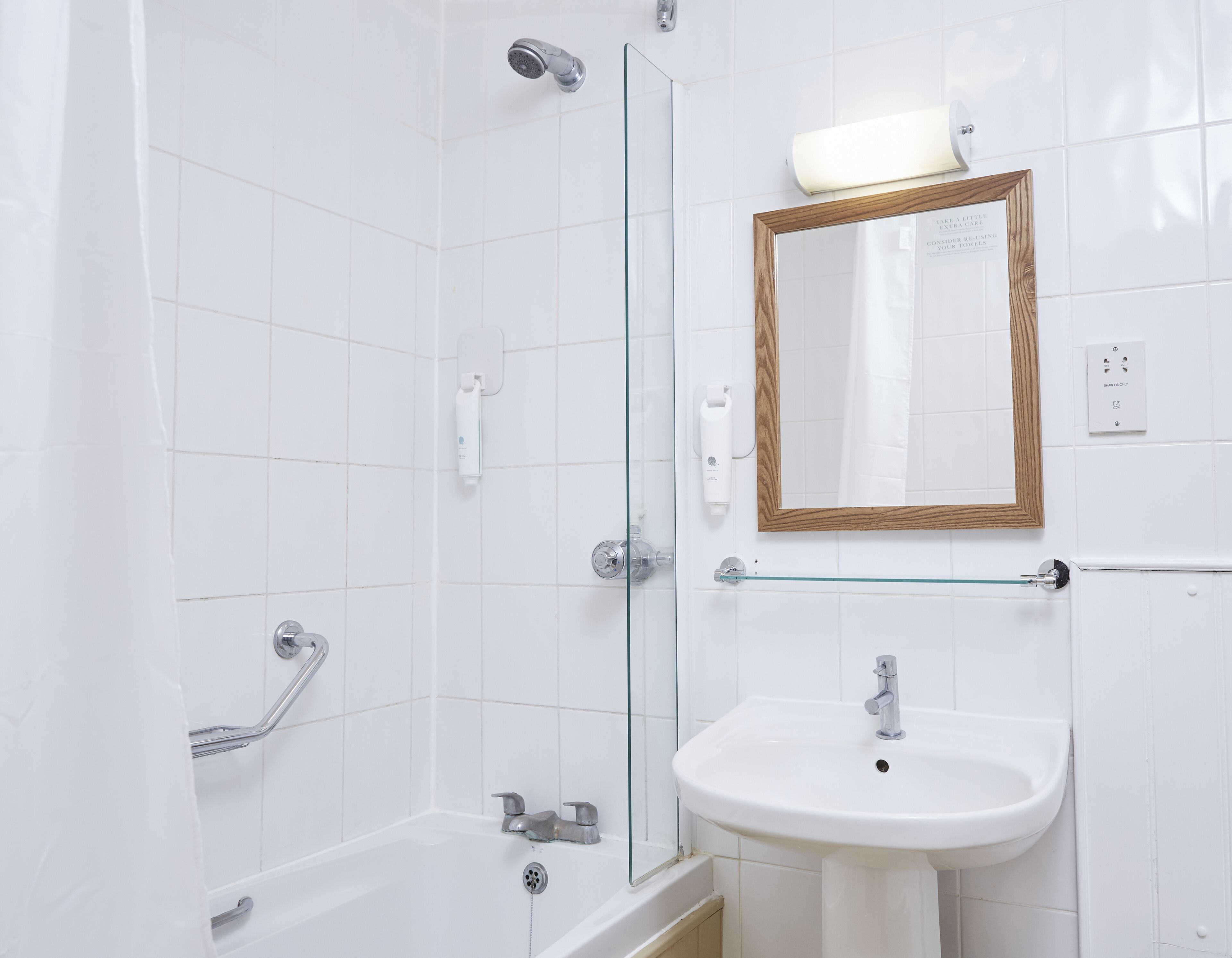 Une salle de bain avec une douche à parois de verre, un lavabo blanc et un miroir encadré en bois.