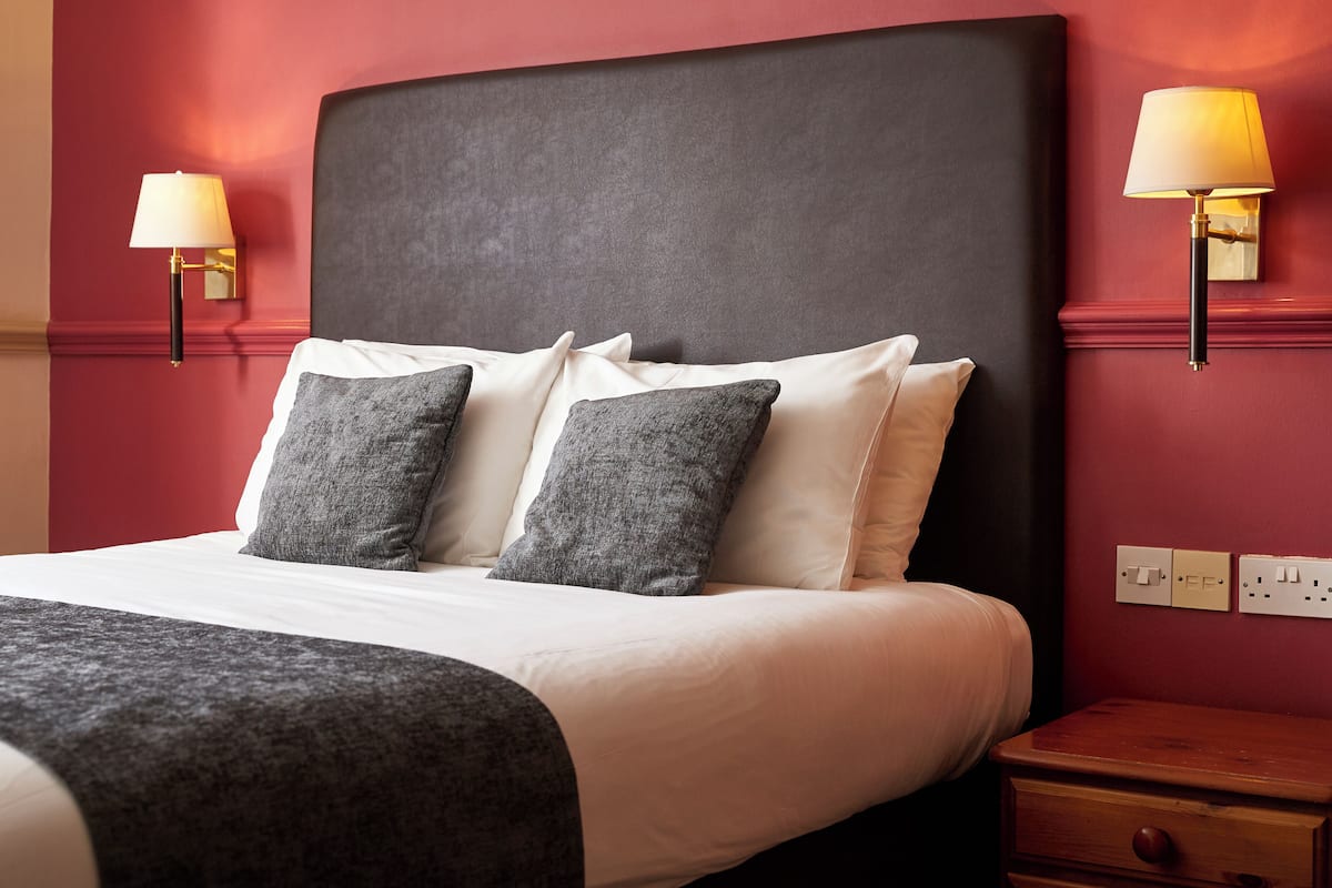 A bed with a black headboard, white linens, and two grey pillows. There are two wall-mounted lamps on either side of the bed.