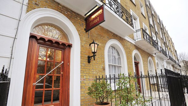 A traditional brick building with a wooden front door, a sign for 'Elmwood Hotel', and potted plants on the sidewalk. - Elmwood Hotel (London)