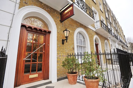 A traditional brick building with a wooden front door, a sign for 'Elmwood Hotel', and potted plants on the sidewalk.