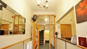 A hotel reception area with a reception desk, a staircase, and a mirror reflecting the interior. - Elmwood Hotel (London)