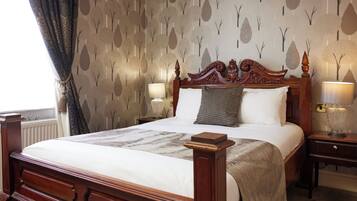 A neatly made bed with a wooden headboard, two bedside lamps, and a patterned wallpaper with tree designs.