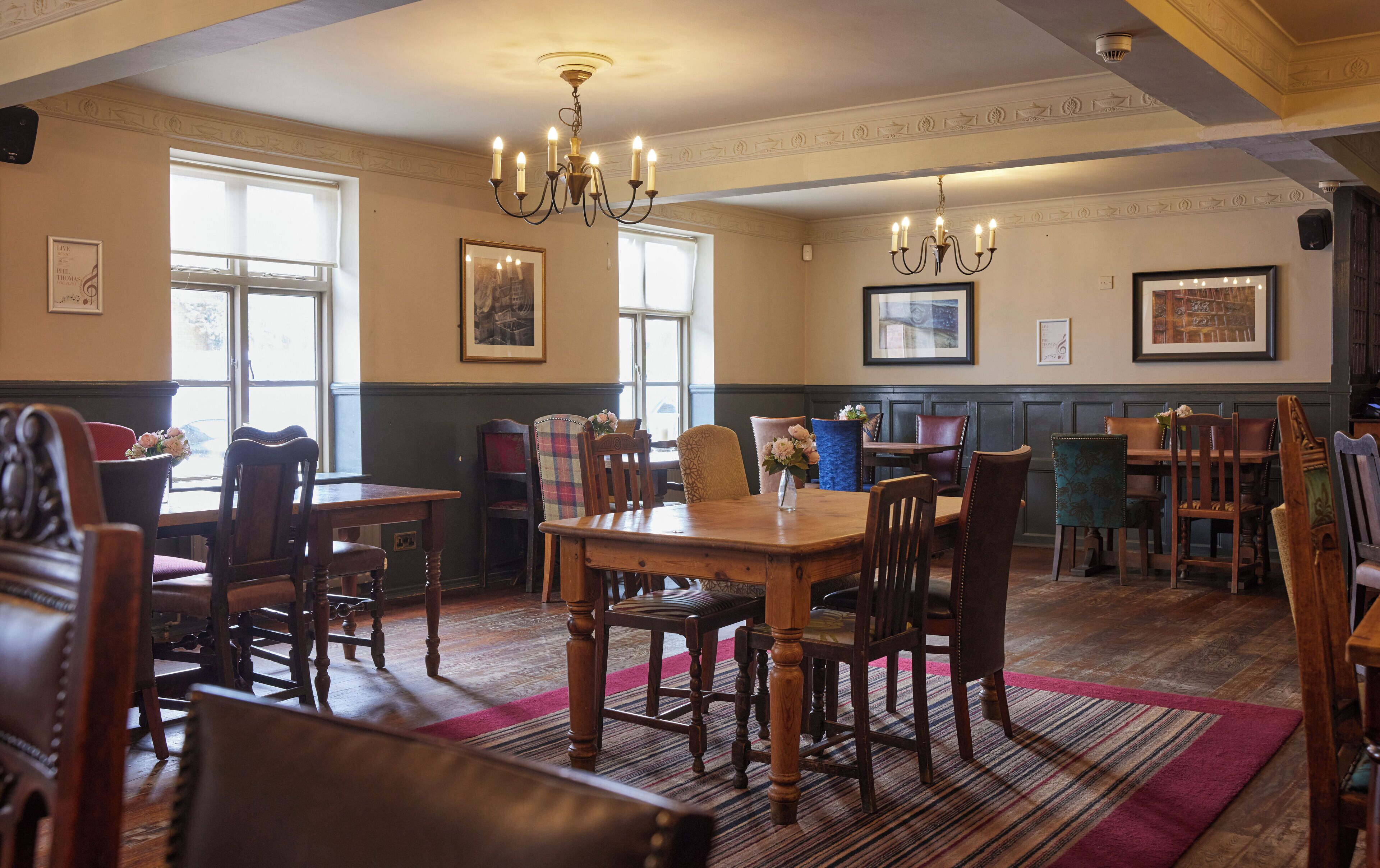 A dining area with wooden tables and chairs, chandeliers, and framed artwork on the walls.