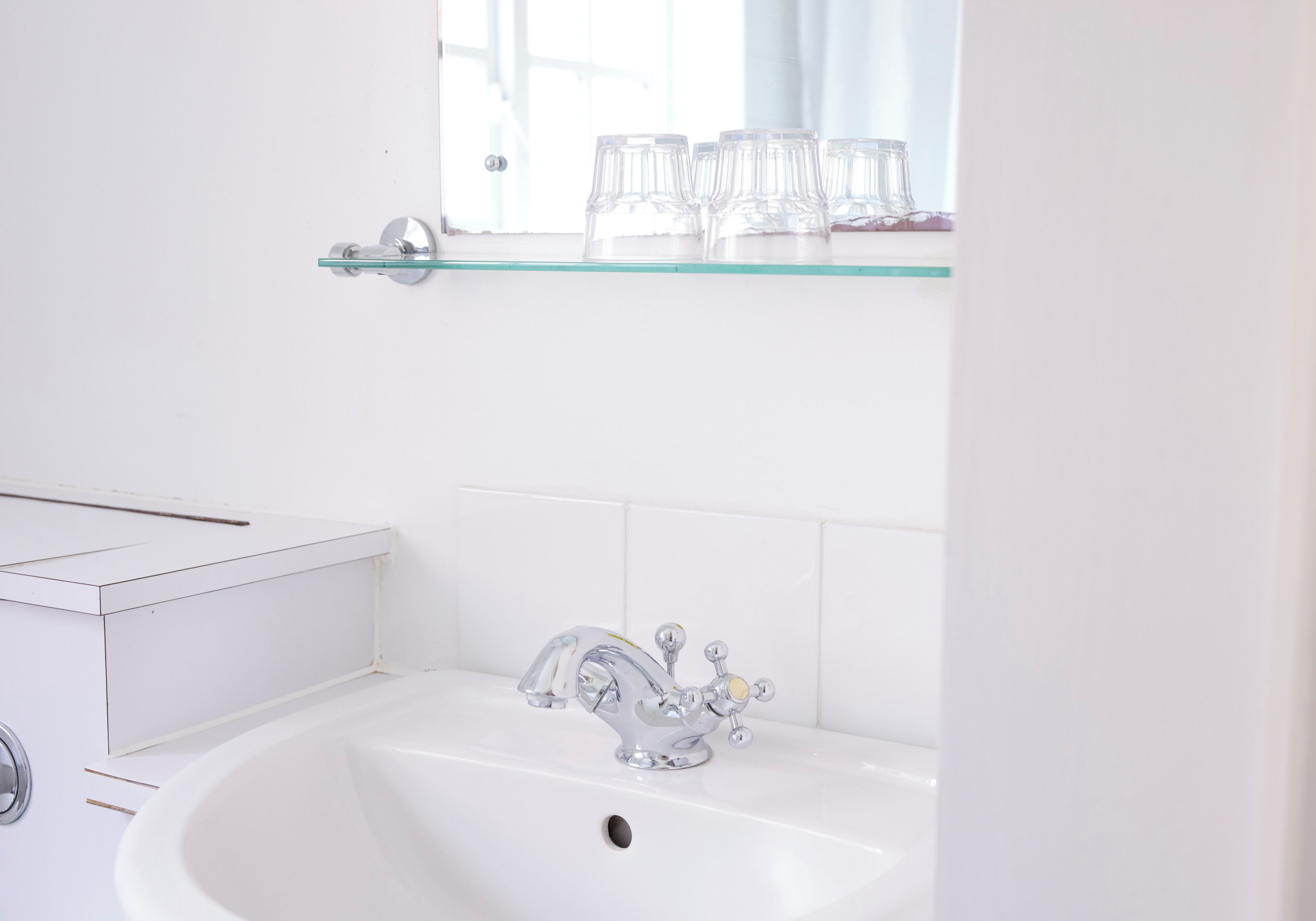 A bathroom with a white sink, chrome faucet, and a glass shelf above the sink.