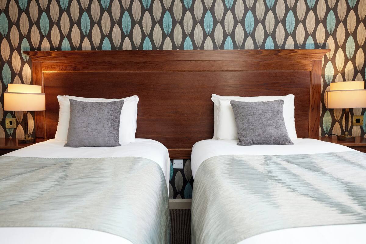 A hotel room with two beds, a wooden headboard, and patterned wallpaper.