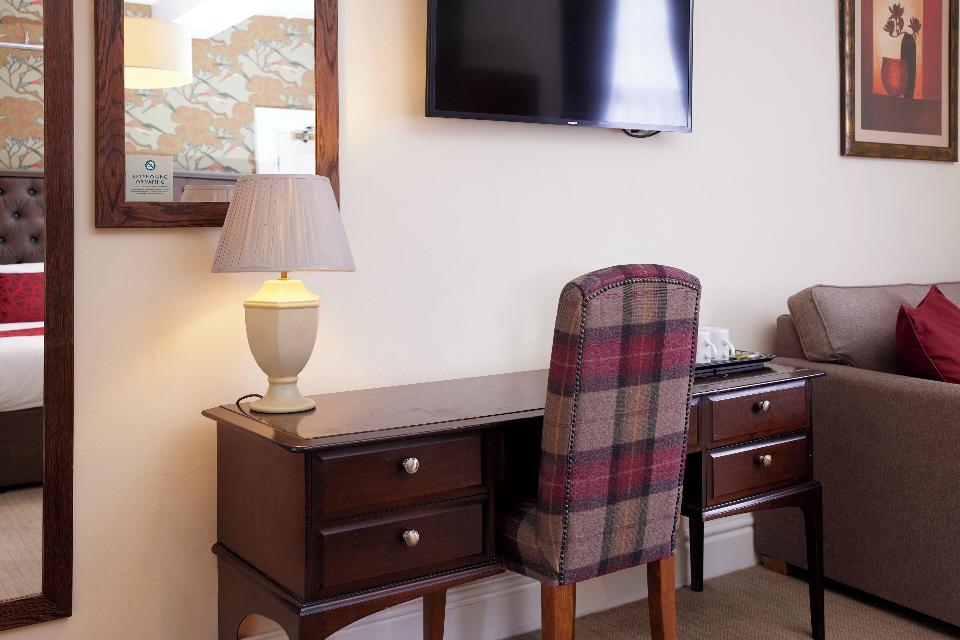 Ein Hotelzimmer mit Schreibtisch, Stuhl und einem an der Wand befestigten Fernseher.