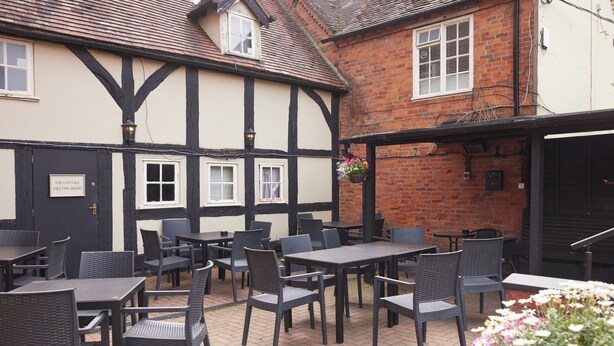 An outdoor seating area with tables and chairs, a sign reading "The Cottage Meeting Room," and a brick building with a black and white facade. - Coleshill Hotel by Greene King Inns (Birmingham)
