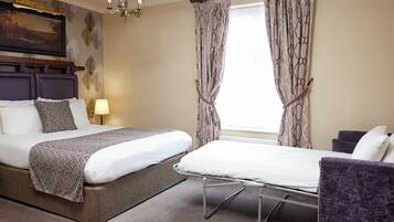 A hotel room with two beds, a headboard, a lamp, and a window with curtains.