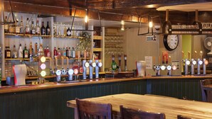 A bar area with multiple taps, shelves of bottles, and a clock on the wall. - Coleshill Hotel by Greene King Inns (Birmingham)