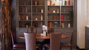 A dining area with a wooden table and four chairs, surrounded by bookshelves filled with books and decorative items. - Coleshill Hotel by Greene King Inns (Birmingham)