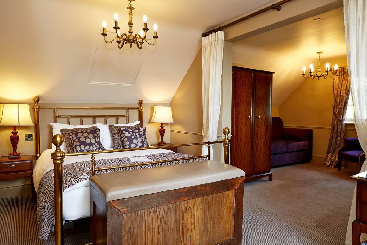 A bedroom with a four-poster bed, a wooden wardrobe, a sofa, and a chandelier.