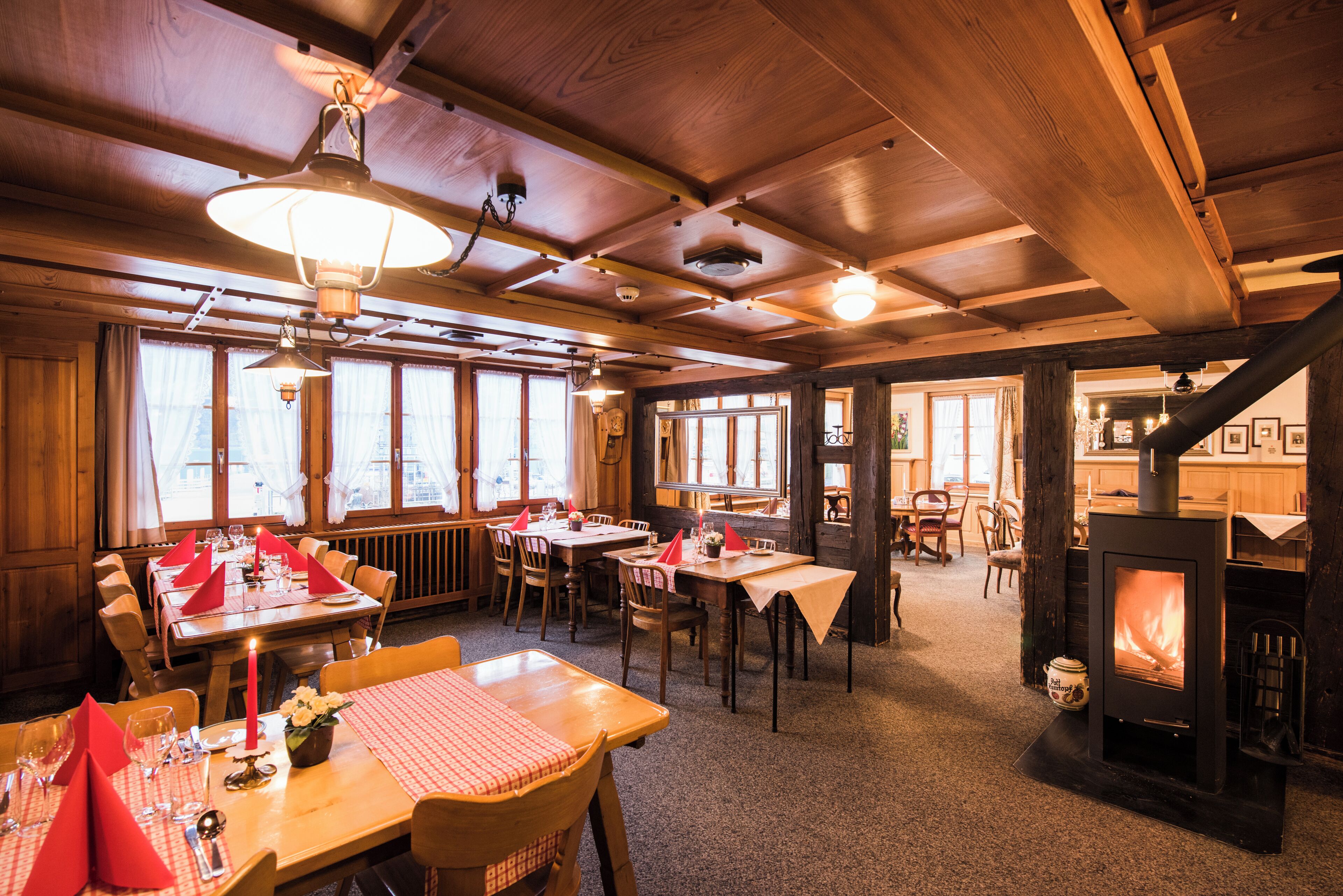 Een gezellig restaurant met houten inrichting, tafels gedekt met rode servetten en een zichtbare open haard.
