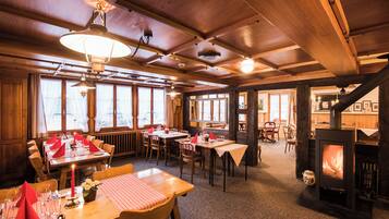 Een gezellig restaurant met houten inrichting, tafels gedekt met rode servetten en een zichtbare open haard.