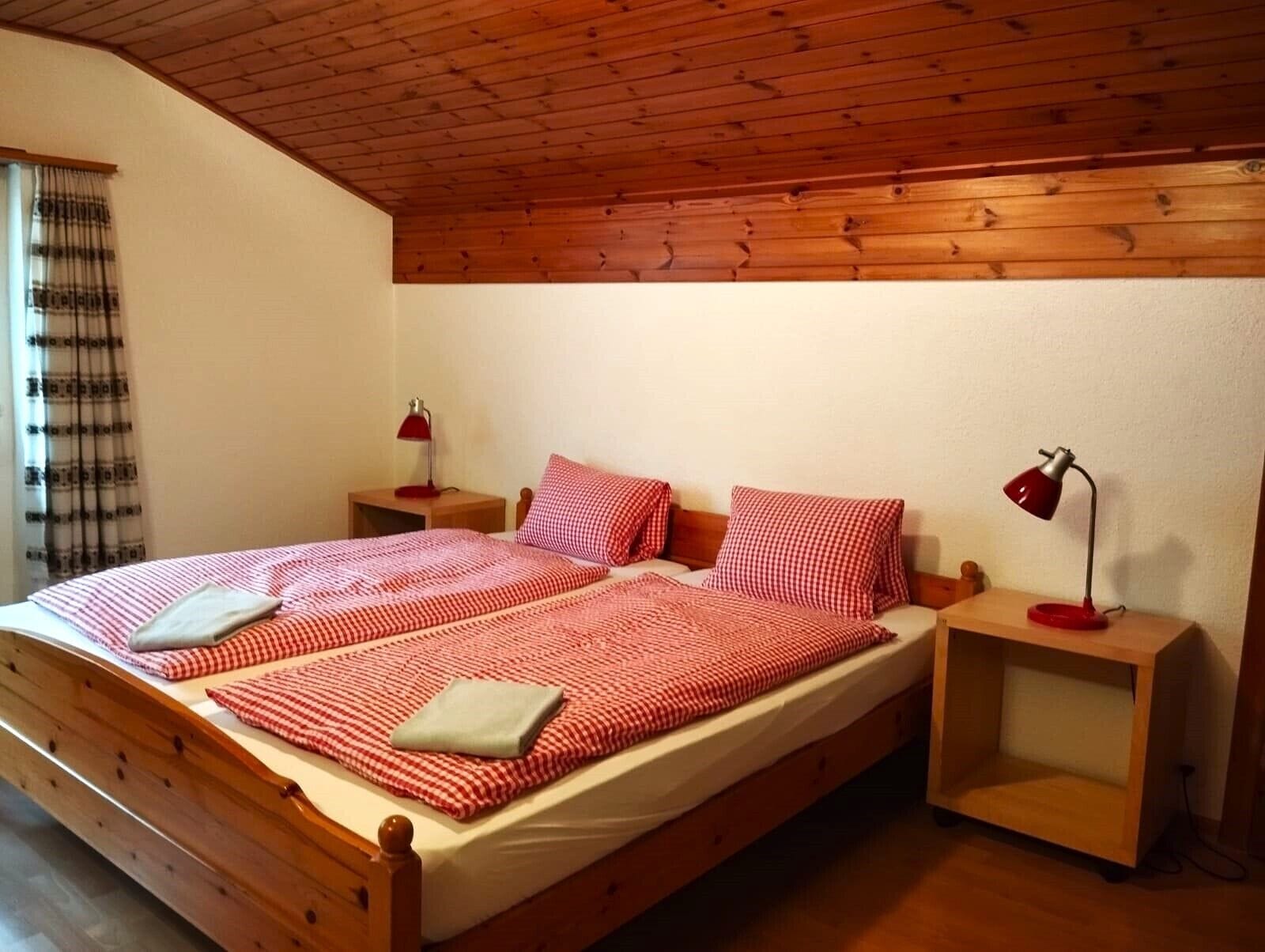 A single bed with a checkered bedspread, two bedside tables with lamps, and a window with curtains.