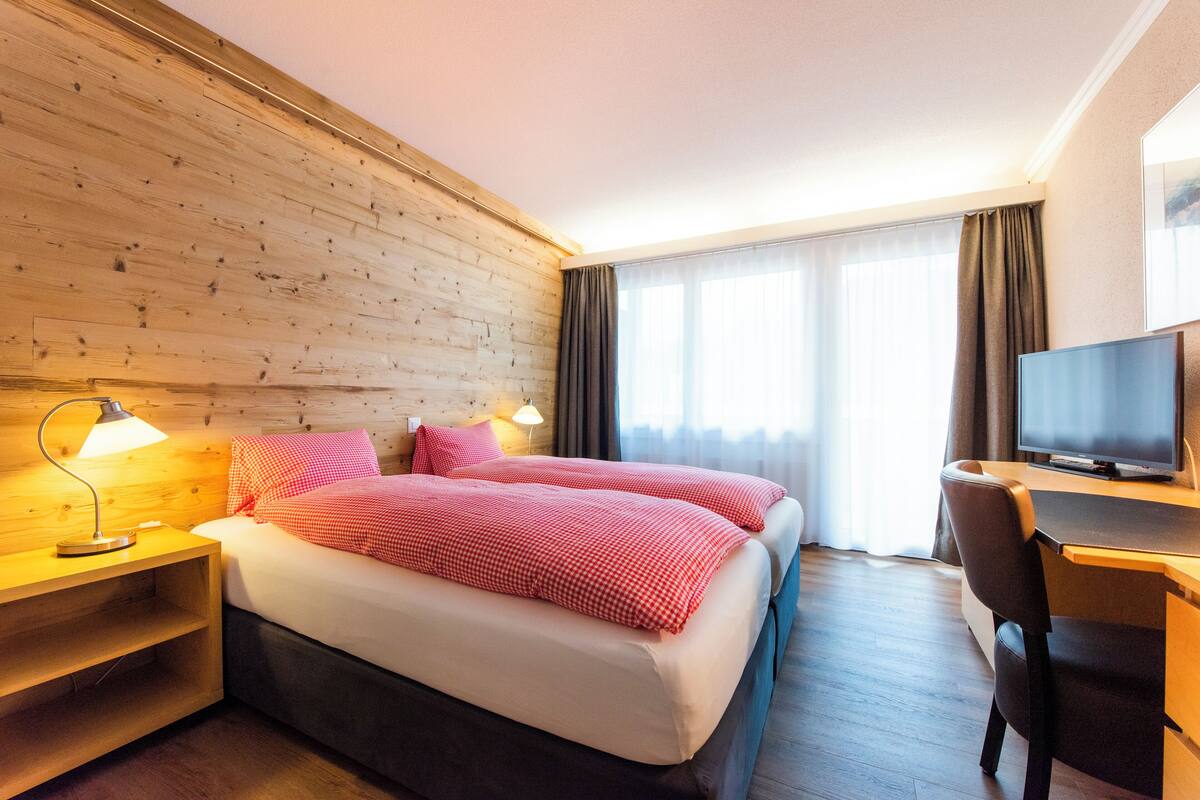 Ein Hotelzimmer mit zwei Betten, einem Schreibtisch, einem Fernseher und einer Holzwand.
