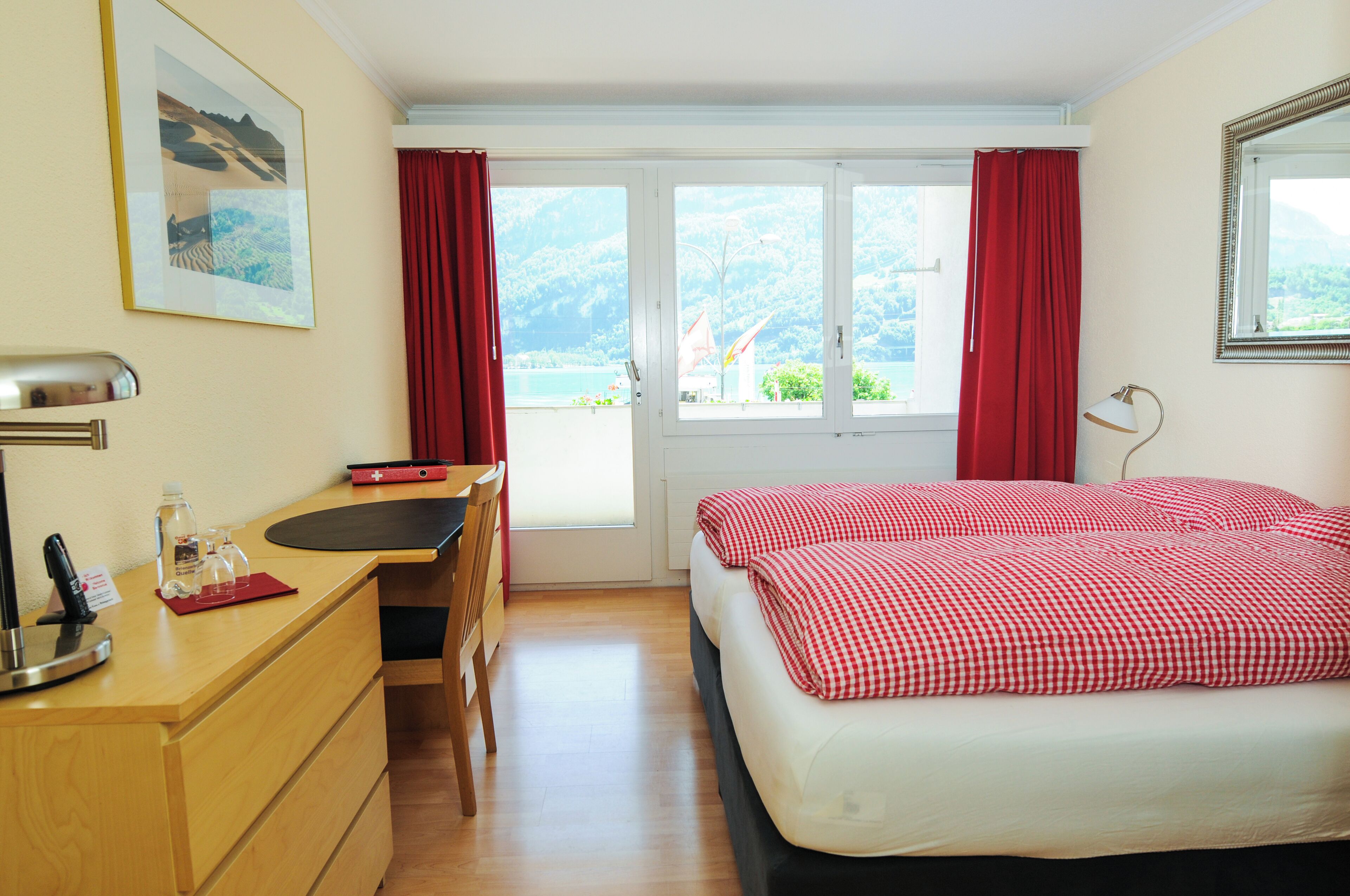 Habitación de hotel con cama, escritorio y silla, ventana con cortinas y un cuadro en la pared.