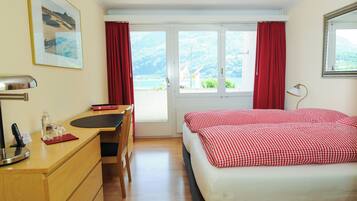 Habitación de hotel con cama, escritorio y silla, ventana con cortinas y un cuadro en la pared.