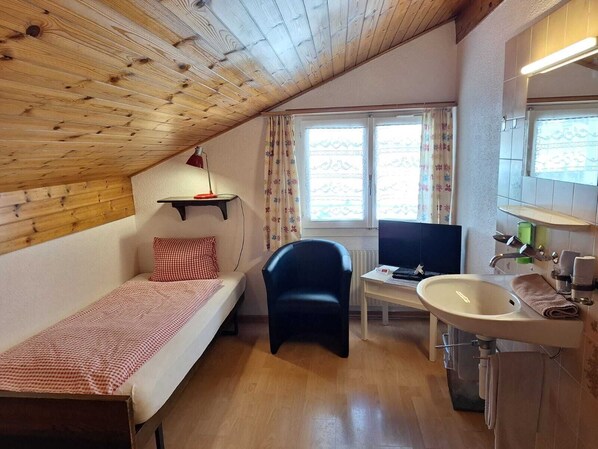 A small, cozy room with a wooden ceiling, a single bed, a desk with a computer, a chair, and a bathroom with a sink and mirror. - Hotel Weisses Kreuz Brienz (Brienz)