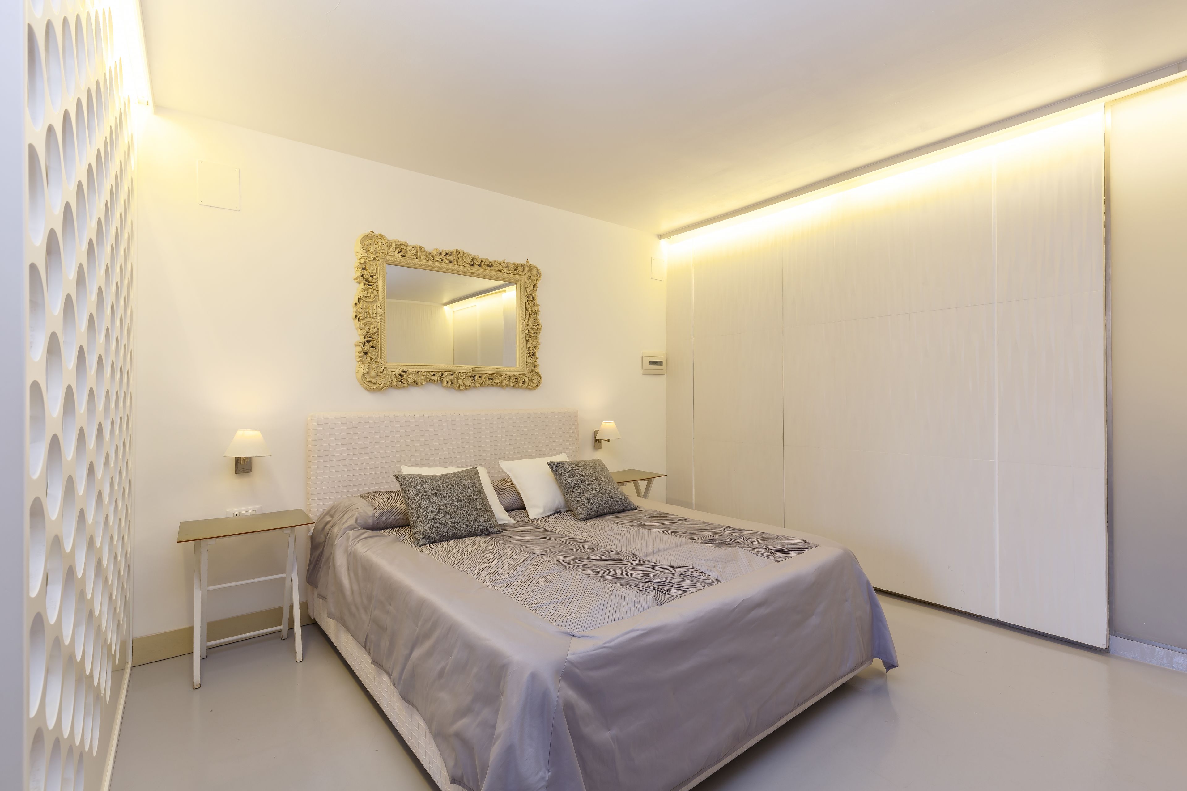 A bedroom with a bed, a nightstand, a wall-mounted mirror, and a wardrobe.